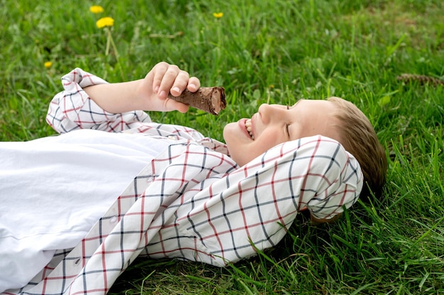 Niño feliz se acuesta en la hierba y come helado de chocolate