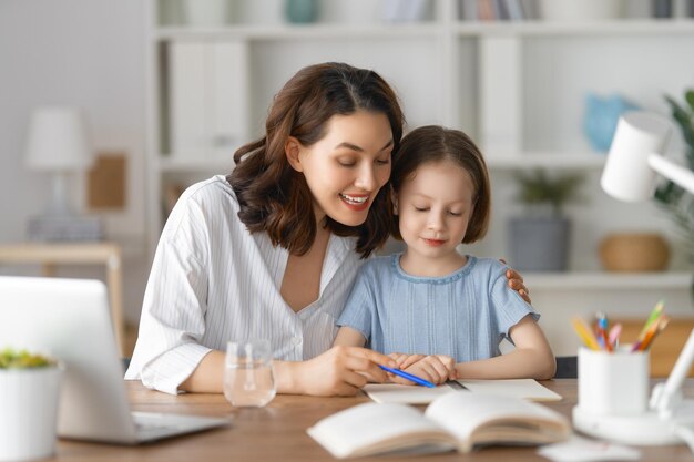 Niño feliz y adulto están sentados en el escritorio Chica haciendo la tarea o educación en línea