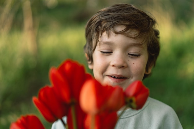 Niño feliz alegre con ramo de flores de tulipanes en la naturaleza