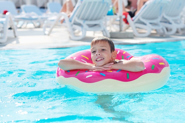 Niño feliz con anillo de vida variado en forma de rosquilla se divierte en la piscina