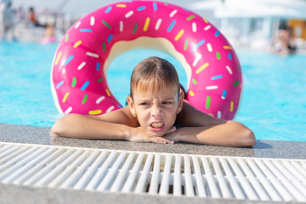 Niño feliz con anillo de vida variado en forma de rosquilla se divierte en la piscina