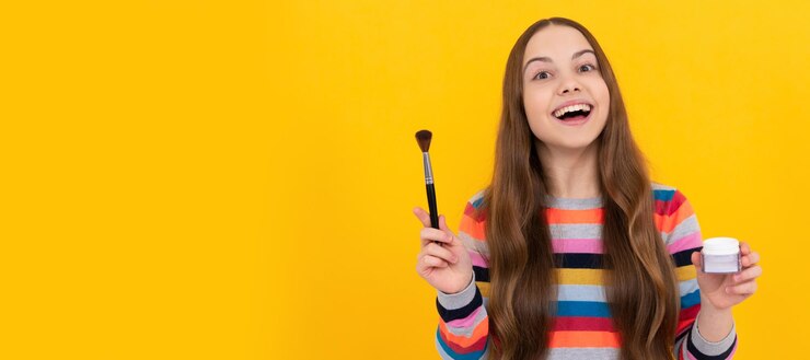 Foto niño feliz aplicar cosméticos con pincel de base maquillaje de fondo amarillo cosméticos para diseño de cartel de niño adolescente banner de maquillaje de niños de belleza con espacio de copia