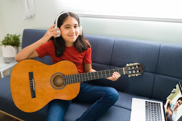 Niño feliz aprendiendo a tocar la guitarra acústica. Niña preadolescente con auriculares sonriendo y disfrutando de sus lecciones de música en línea