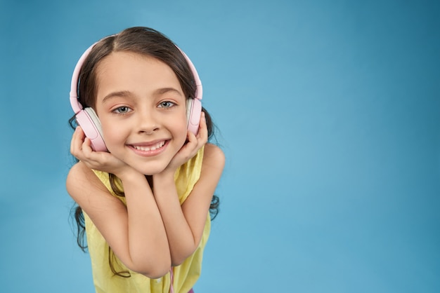 Niño feliz en auriculares rosa sonriendo, mirando a cámara.