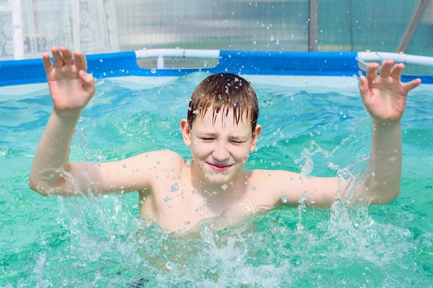 Niño feliz se baña en la piscina con salpicaduras en un caluroso día de verano