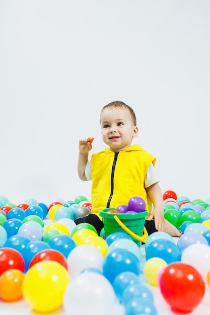 Niño feliz con bolas de colores en el grupo de juegos de niños el niño sonríe escondiéndose en las bolas