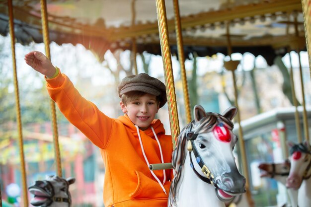 Un niño feliz cabalga en un caballo de carrusel antiguo y agita la mano recuerdos de la infancia