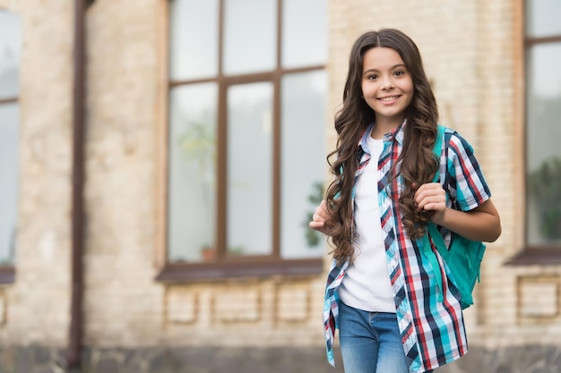 Niño feliz con cabello largo ondulado en estilo de moda casual llevar bolsa de viaje urbano al aire libre viajar