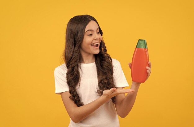 Niño feliz con cabello largo que presenta el producto de la propuesta de producto de botella de champú