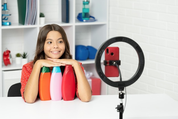 Niño feliz con cabello largo y rizado haciendo una revisión del acondicionador para el cabello para bloguear la infancia