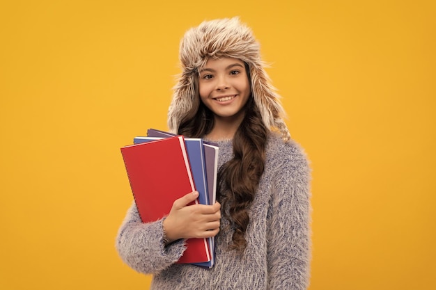 Niño feliz cabello largo con sombrero con cuaderno sobre educación de fondo amarillo