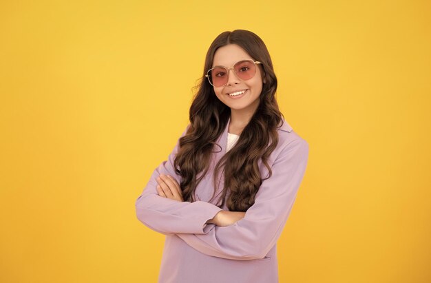 Niño feliz con cabello rizado en elegante chaqueta morada y gafas de sol sobre fondo amarillo felicidad