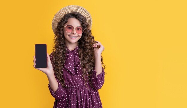 Niño feliz con cabello rizado que presenta la pantalla del teléfono inteligente con espacio de copia