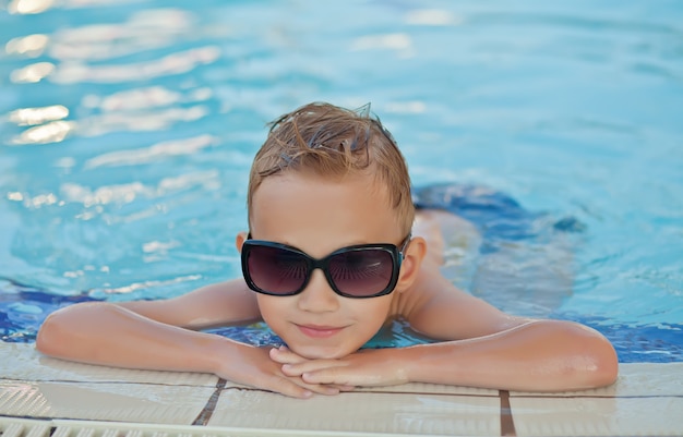 Niño feliz con cabello rubio sonriendo sentado en la piscina