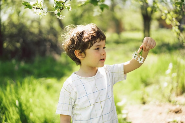 Niño feliz caminando en el jardín de primavera Niño jugando con la rama de un cerezo y divirtiéndose Niño explorando la naturaleza Bebé divirtiéndose Actividad de primavera para niños curiosos