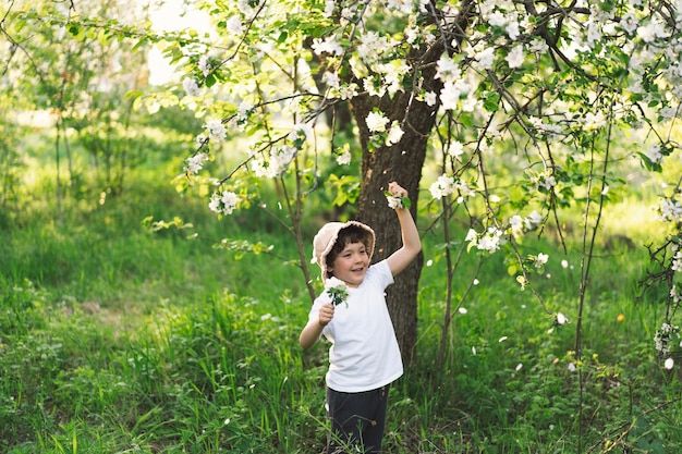 Niño feliz caminando en el jardín de primavera Niño jugando con la rama de un manzano y divirtiéndose Niño explorando la naturaleza Bebé divirtiéndose Actividad de primavera para niños curiosos