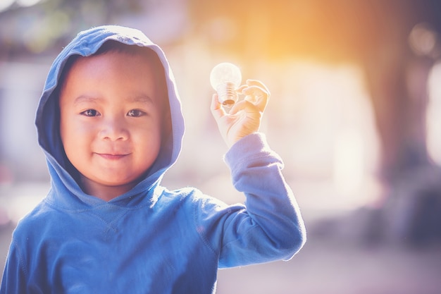 niño feliz en capucha azul sosteniendo una bombilla en la mano.