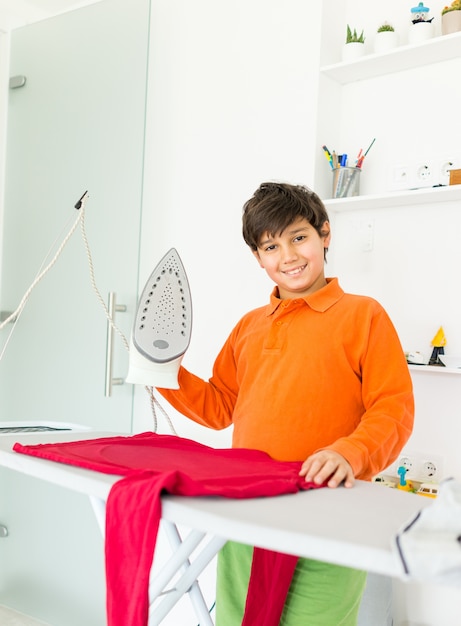 Niño feliz en casa planchando ropa