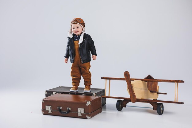 Un niño feliz con un casco y una chaqueta de piloto se encuentra cerca de un avión de madera Retrato de un niño piloto un niño con una chaqueta de cuero Juguetes de madera Avión ecológico del árbol