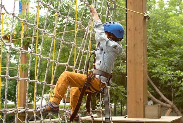 Niño feliz con casco y equipo de protección disfruta de clases en el parque de aventuras de escalada en un día de verano