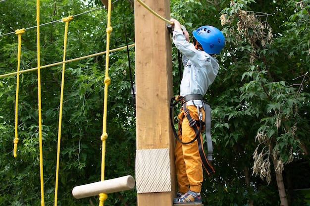 Niño feliz con casco y equipo de protección disfruta de clases en el parque de aventuras de escalada en un día de verano