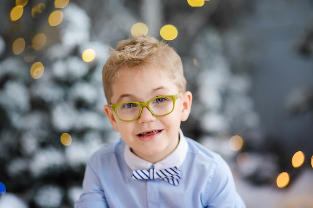 El niño feliz de CCharming está sentado en casa, árbol cubierto de invierno nevado