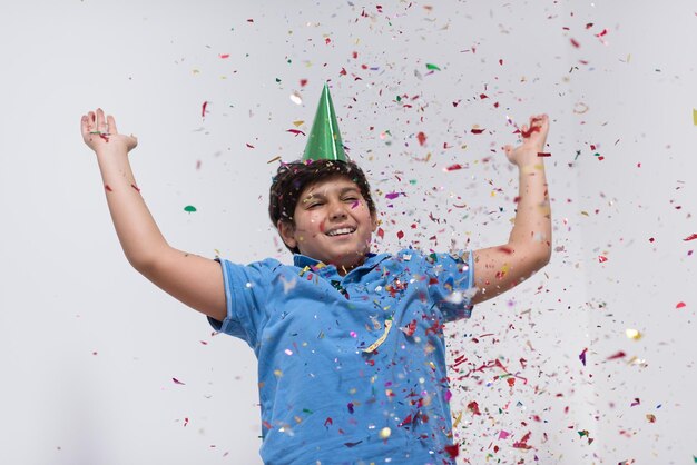 Niño feliz celebrando la fiesta con confeti que sopla