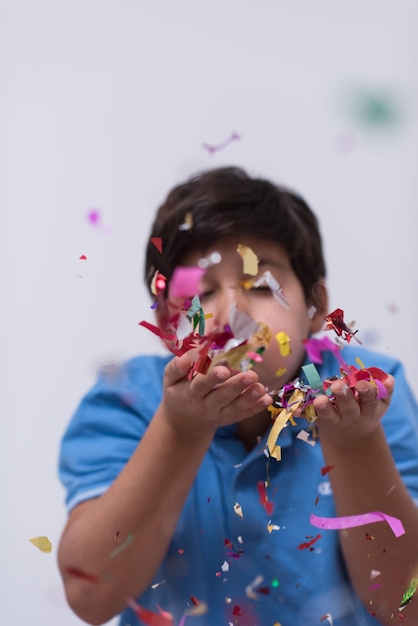 Niño feliz celebrando la fiesta con confeti que sopla