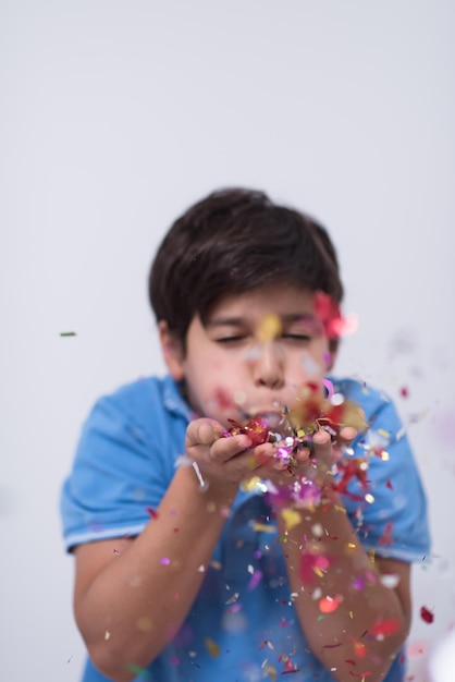 Niño feliz celebrando la fiesta con confeti que sopla