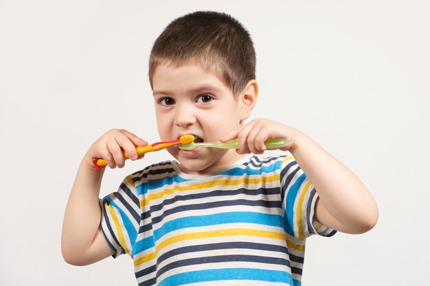 Un niño feliz se cepilla los dientes con dos cepillos de dientes.