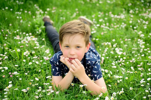 Niño feliz en el césped. Niño lindo disfrutando de flor de campo. Niño soñando.