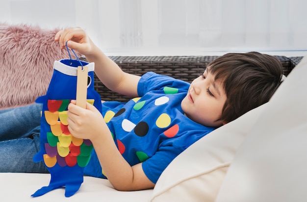 Niño feliz de clave alta quedarse en casa acostado en el sofá jugando Koinobori (serpentinas de carpas), niño chico haciendo cometa de pescado japonés