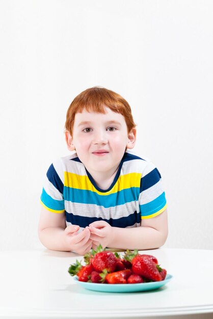 un niño feliz come fresas maduras, un retrato cerrado de un niño de seis años mientras come un postre de bayas