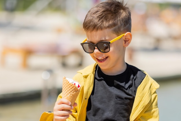 Un niño feliz come helado en un cono de waffle en verano en un paseo