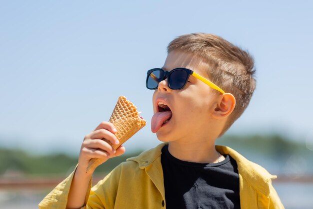 Un niño feliz come helado en un cono de waffle en verano en un paseo
