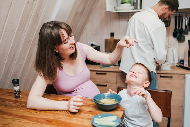 Niño feliz come pasta en la cocina con su familia