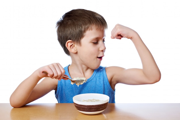 Niño feliz comiendo gachas en la mesa aislada