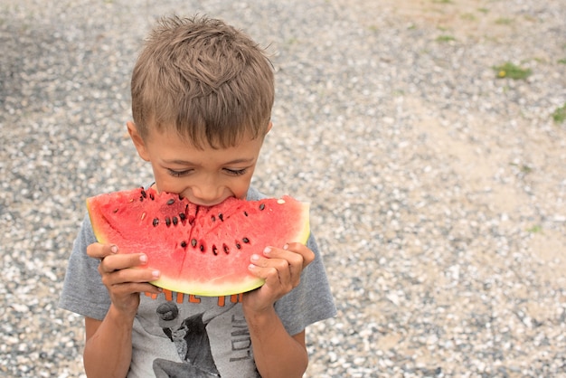 Niño feliz comiendo una sandía madura.