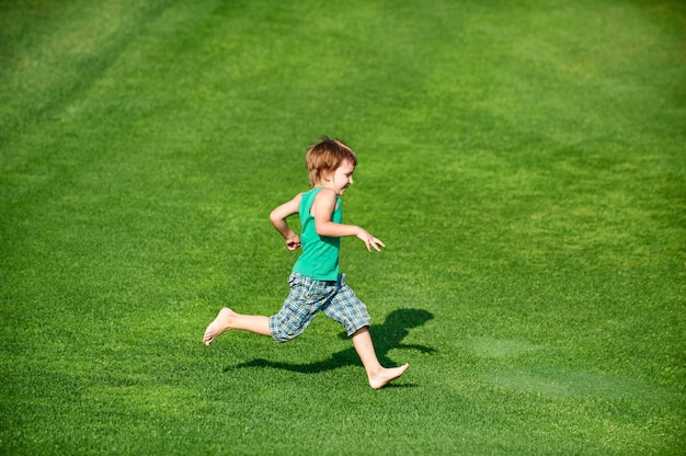 Niño feliz corriendo en el campo de golf verde en un día soleado