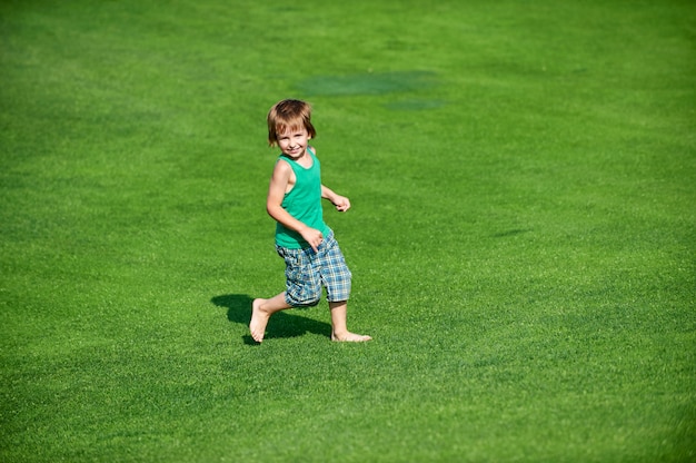 Niño feliz corriendo en el campo de golf verde en un día soleado