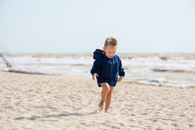 Niño feliz corriendo en chaqueta sobre arena.