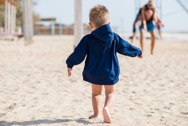 Niño feliz corriendo en chaqueta sobre arena.