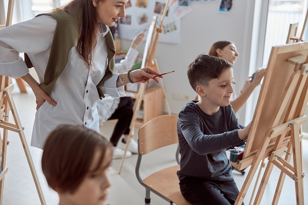 Niño feliz creativo joven está haciendo un dibujo mientras el maestro lo ayuda