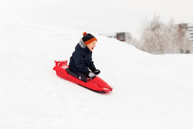 niño feliz deslizándose en trineo por la colina de nieve en invierno