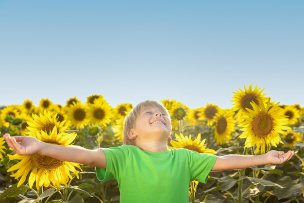 Niño feliz divirtiéndose en el campo de primavera de girasoles Retrato al aire libre de niño contra el fondo del cielo azul