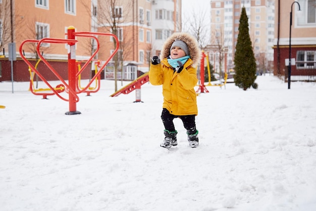 Niño feliz divirtiéndose en la nieve en la ciudad Diversión de invierno afuera Niño en chaqueta de invierno naranja brillante Concepto de vacaciones de invierno