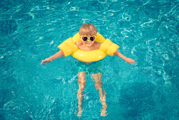 Niño feliz divirtiéndose en las vacaciones de verano Niño jugando en la piscina Niño con anillo inflable amarillo Concepto de estilo de vida activo y saludable