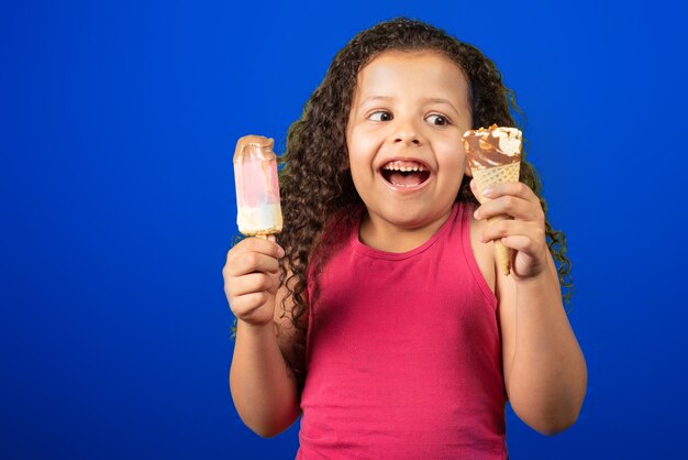 Niño feliz con dos helados en la mano con mesa azul, enfoque selectivo.