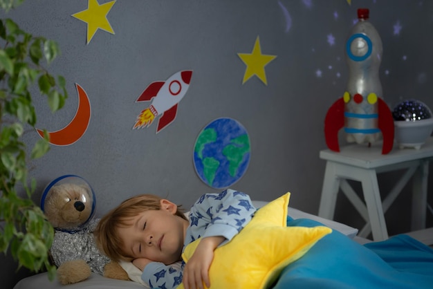 Niño feliz durmiendo con cohete de juguete y oso de peluche. El niño finge ser astronauta. Concepto de imaginación y sueño de los niños.