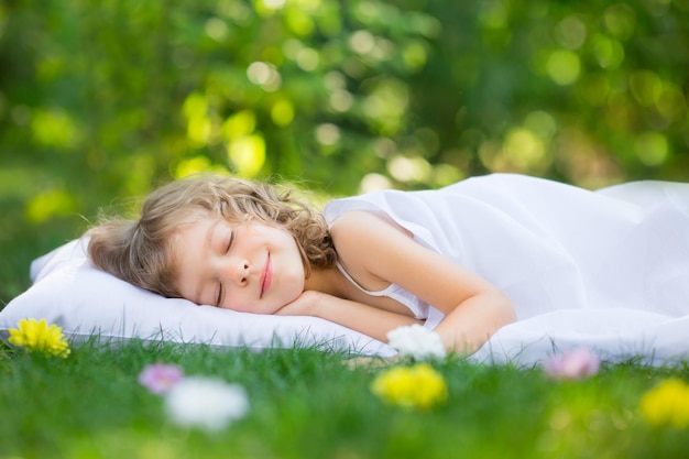 Niño feliz durmiendo en la hierba verde al aire libre en el jardín de primavera